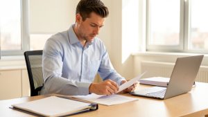 Un homme prépare des documents administratifs vierges sur un bureau lumineux, avec un ordinateur portable et un dossier professionnel.